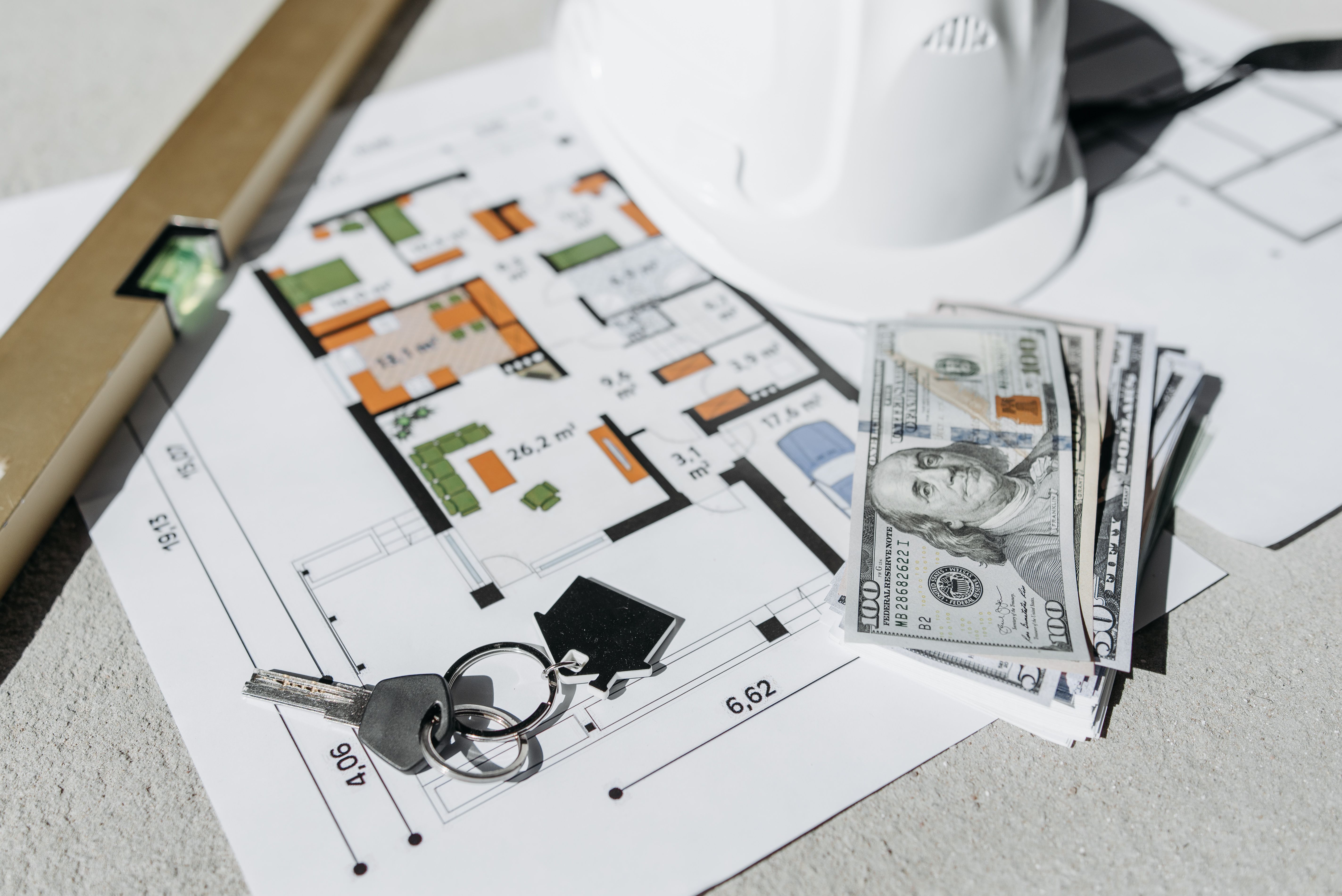 Floor plan with cash, keys, and hard hat symbolizing property investment and planning